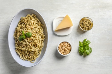 Plate of delicious basil pesto pasta with ingredients on white background, flat lay