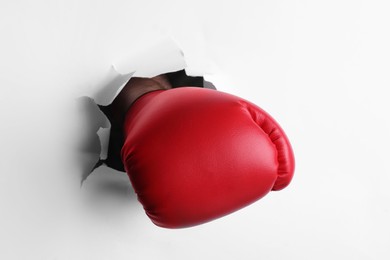 Man breaking through white paper with boxing glove, closeup