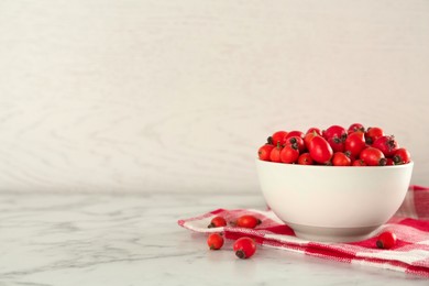 Ceramic bowl with rose hip berries and napkin on white marble table, space for text. Cooking utensil