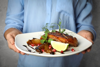 Photo of Woman holding plate with grilled duck breast on grey background, closeup