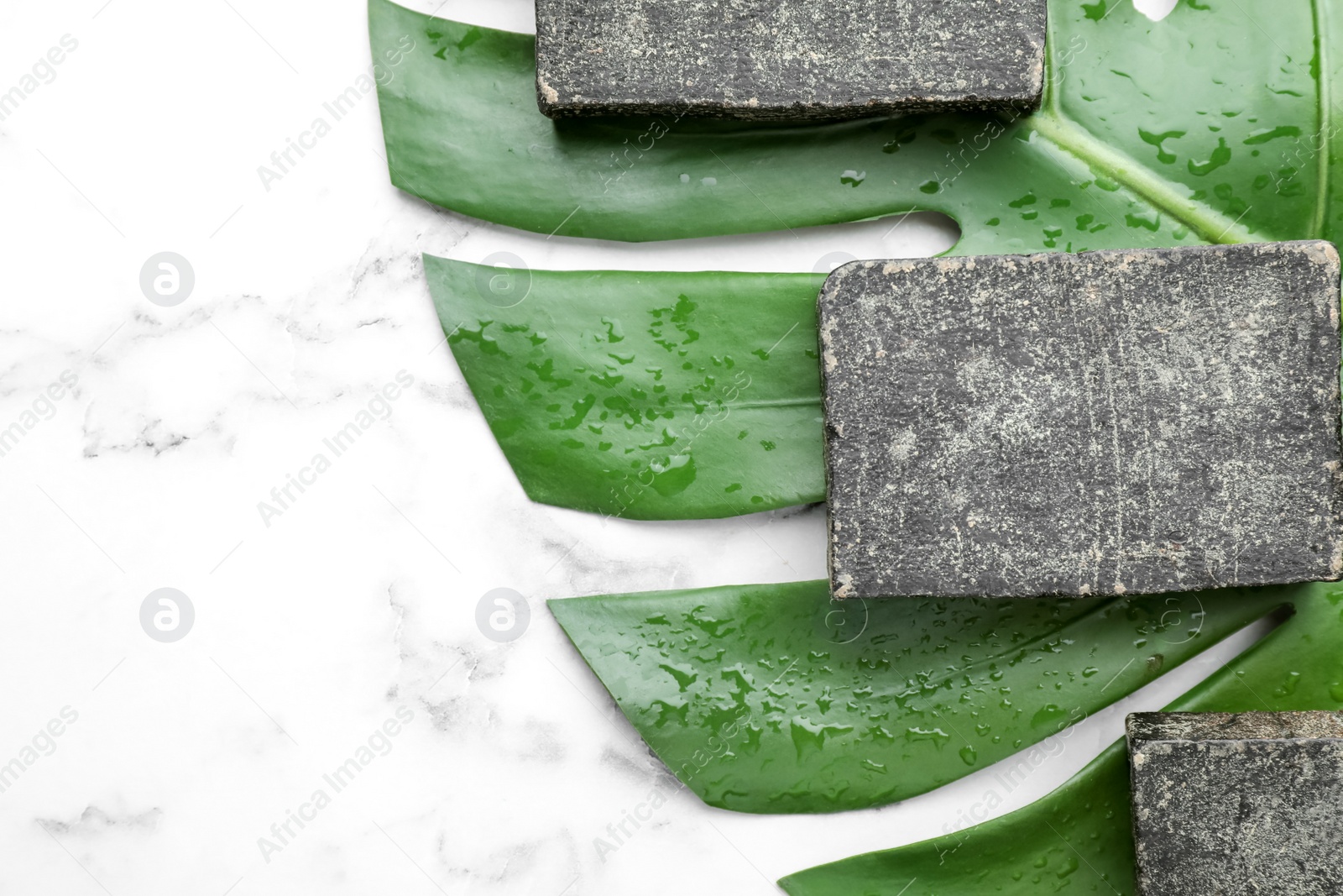 Photo of Natural tar soap and green leaf on white marble table, flat lay