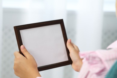 Photo of Little girl holding empty photo frame indoors, closeup