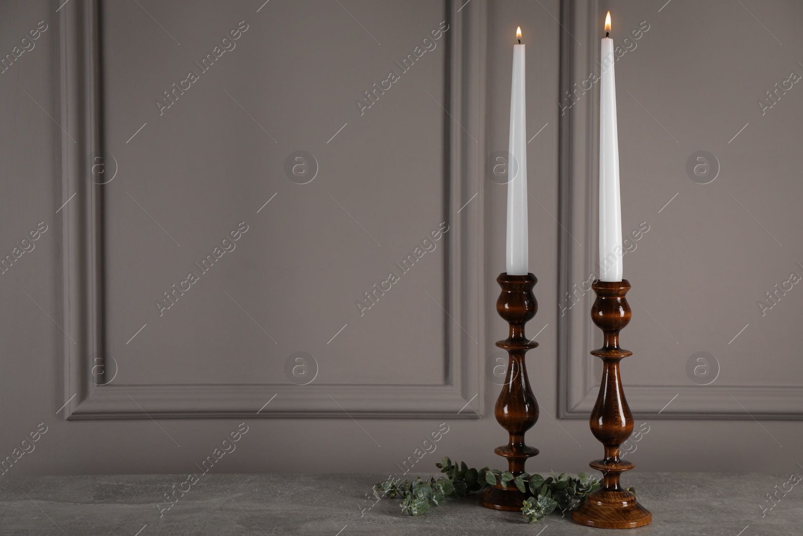 Photo of Elegant candlesticks with burning candles and eucalyptus on grey table. Space for text