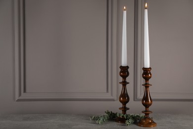 Photo of Elegant candlesticks with burning candles and eucalyptus on grey table. Space for text