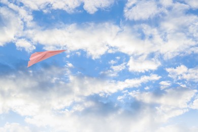 Image of Pink paper plane flying in blue sky with clouds