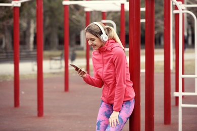 Photo of Young woman with headphones taking break on sports ground