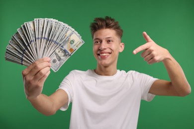 Photo of Happy man pointing at dollar banknotes on green background