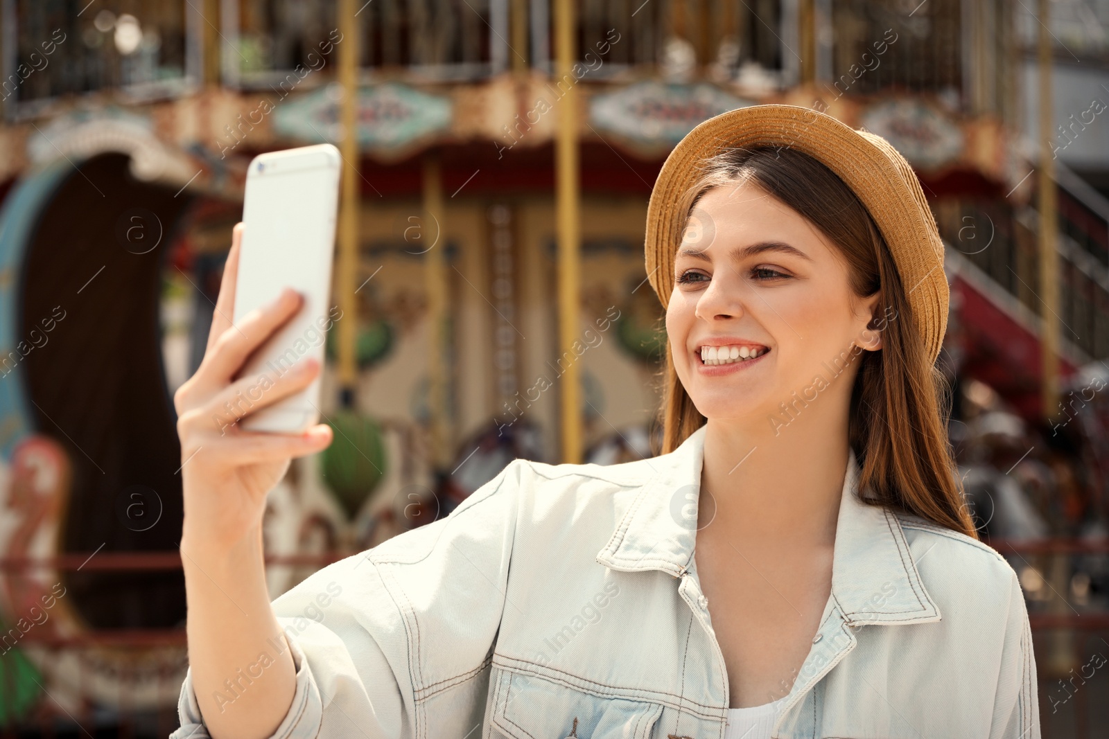 Photo of Young pretty woman taking selfie near carousel in amusement park