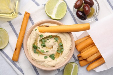 Delicious hummus with grissini sticks, lime and olives on light grey table, flat lay