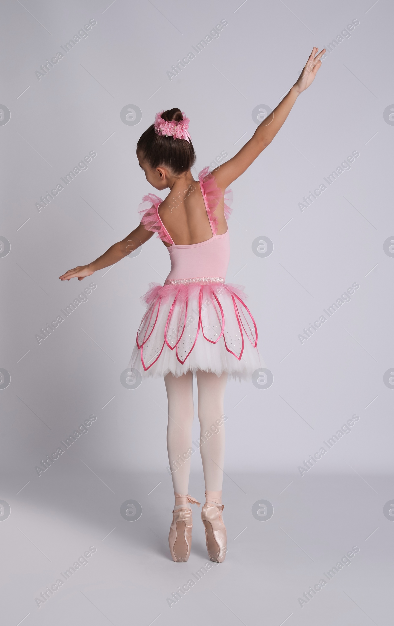 Photo of Beautifully dressed little ballerina dancing on grey background, back view
