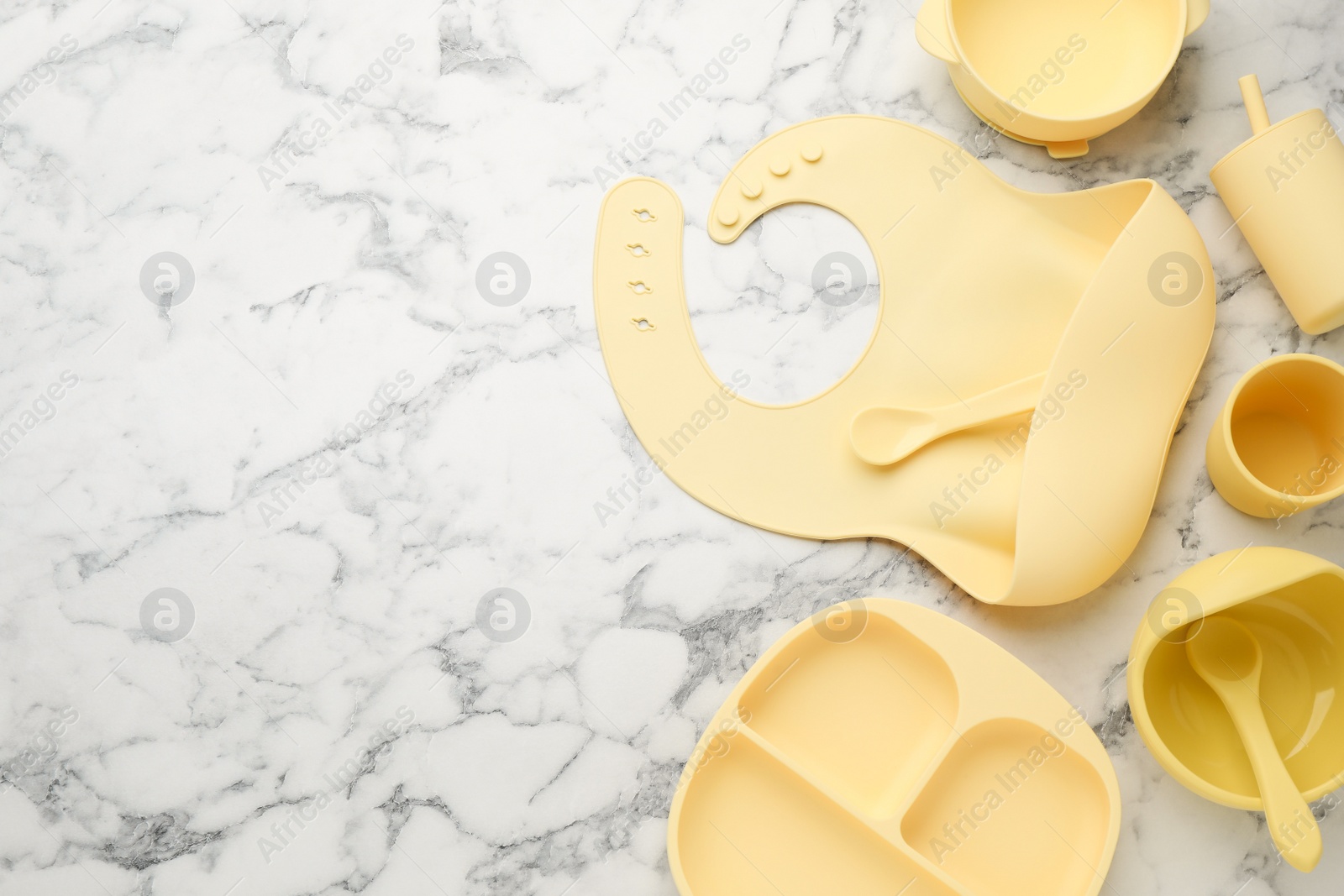 Photo of Flat lay composition with silicone baby bib and plastic dishware on white marble background. Space for text