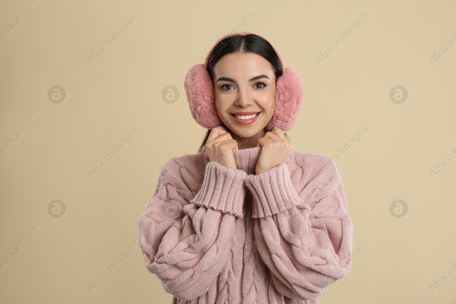 Photo of Beautiful young woman wearing earmuffs on beige background