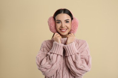 Beautiful young woman wearing earmuffs on beige background