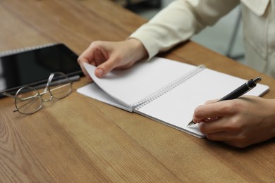 Photo of Left-handed woman writing in notebook at wooden table, closeup