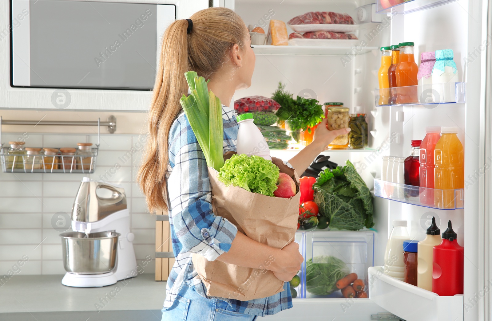 Photo of Woman putting products into refrigerator in kitchen