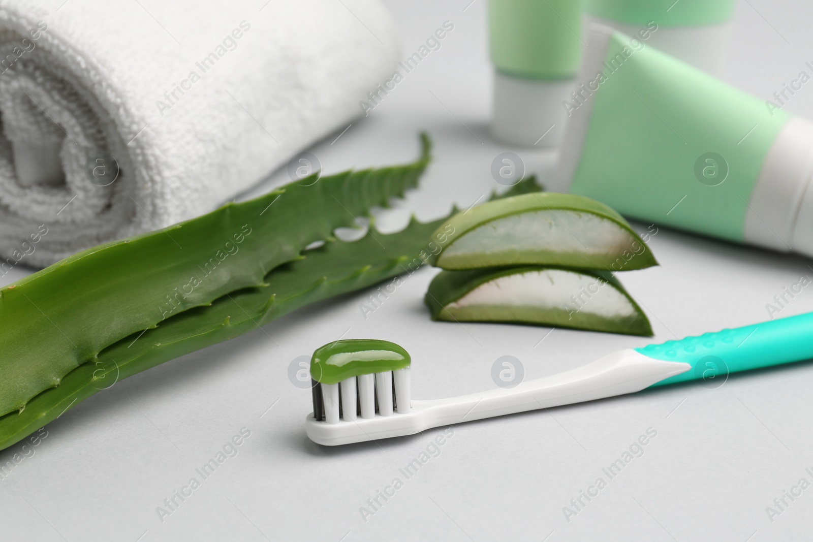 Photo of Toothbrush with toothpaste, towel and fresh aloe on light grey background, closeup