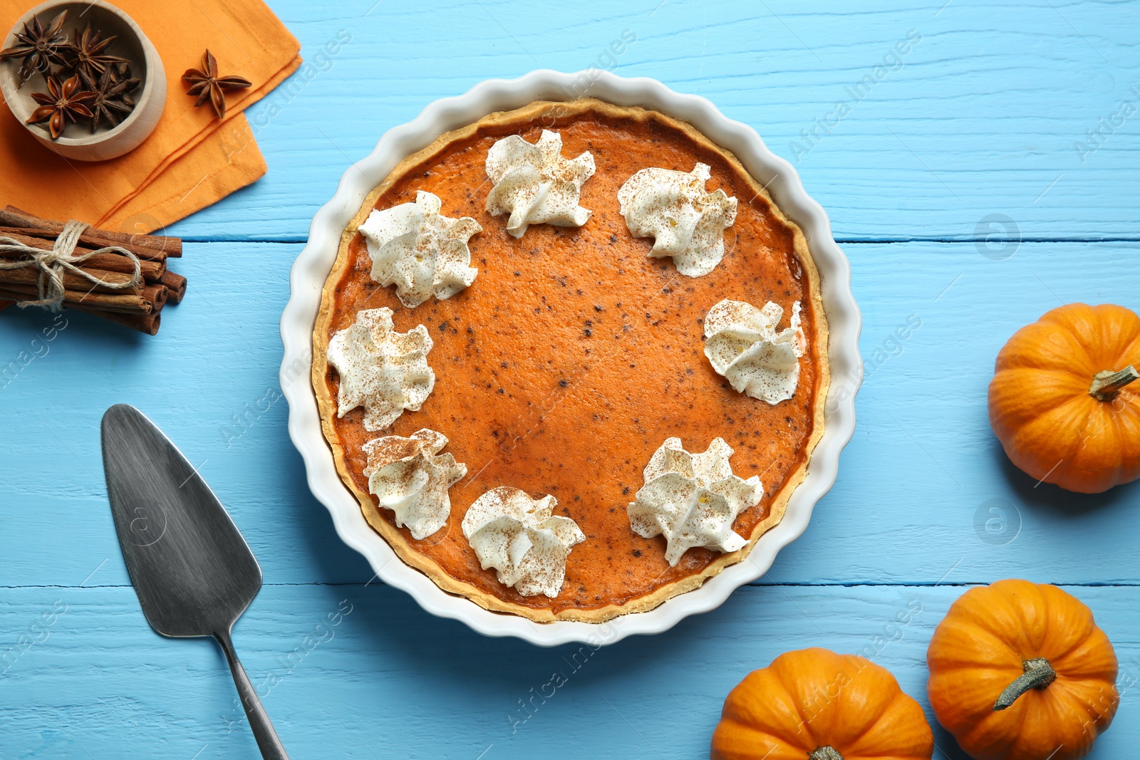 Photo of Delicious pumpkin pie with whipped cream and spices on light blue wooden table, flat lay