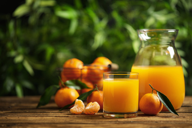 Photo of Glass and bottle of fresh tangerine juice and fruits on wooden table. Space for text