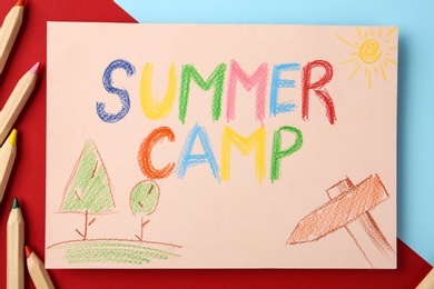 Photo of Paper with written text SUMMER CAMP, drawings and different pencils on color background, flat lay