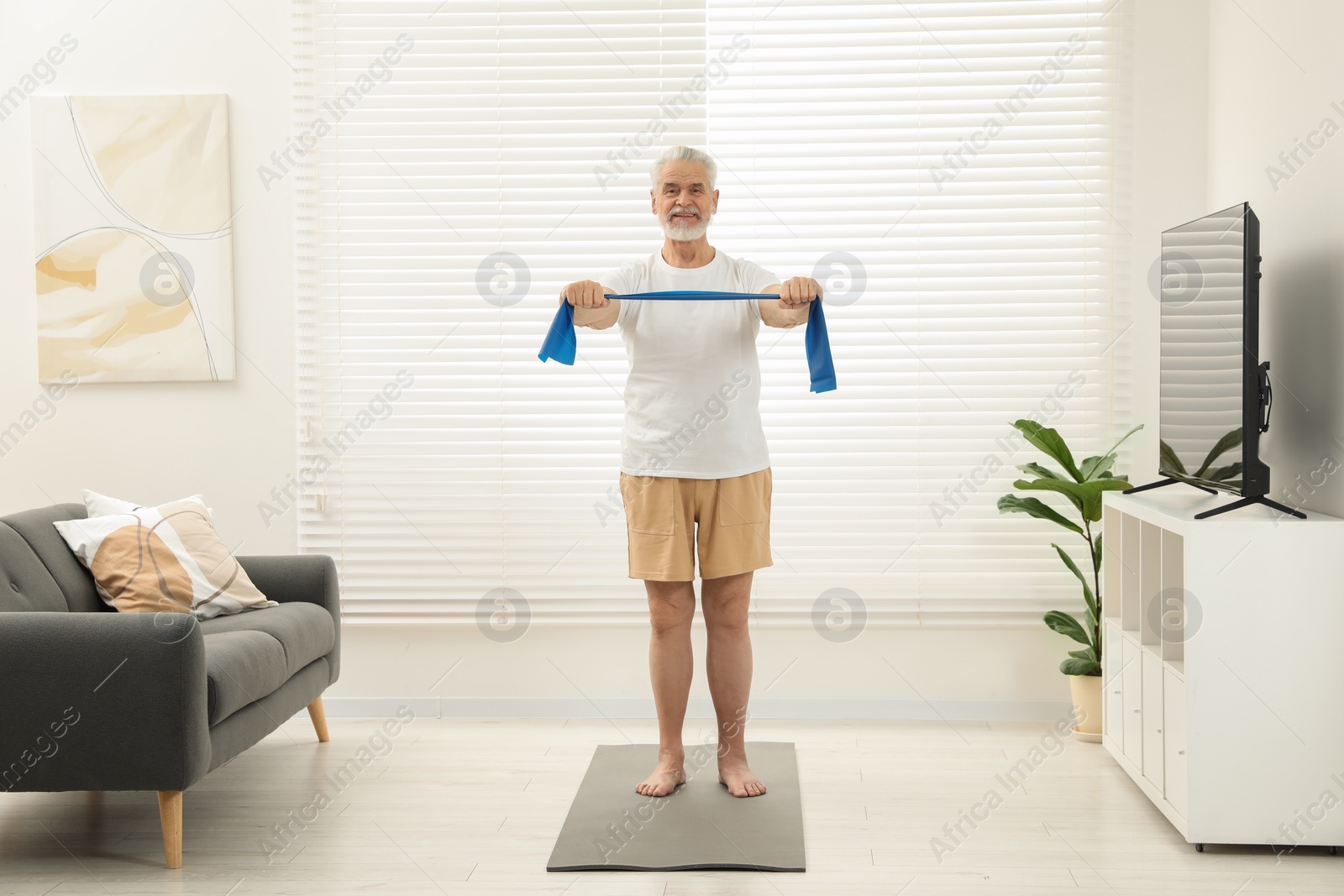 Photo of Senior man doing exercise with fitness elastic band on mat at home