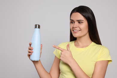 Young woman with thermo bottle on light grey background