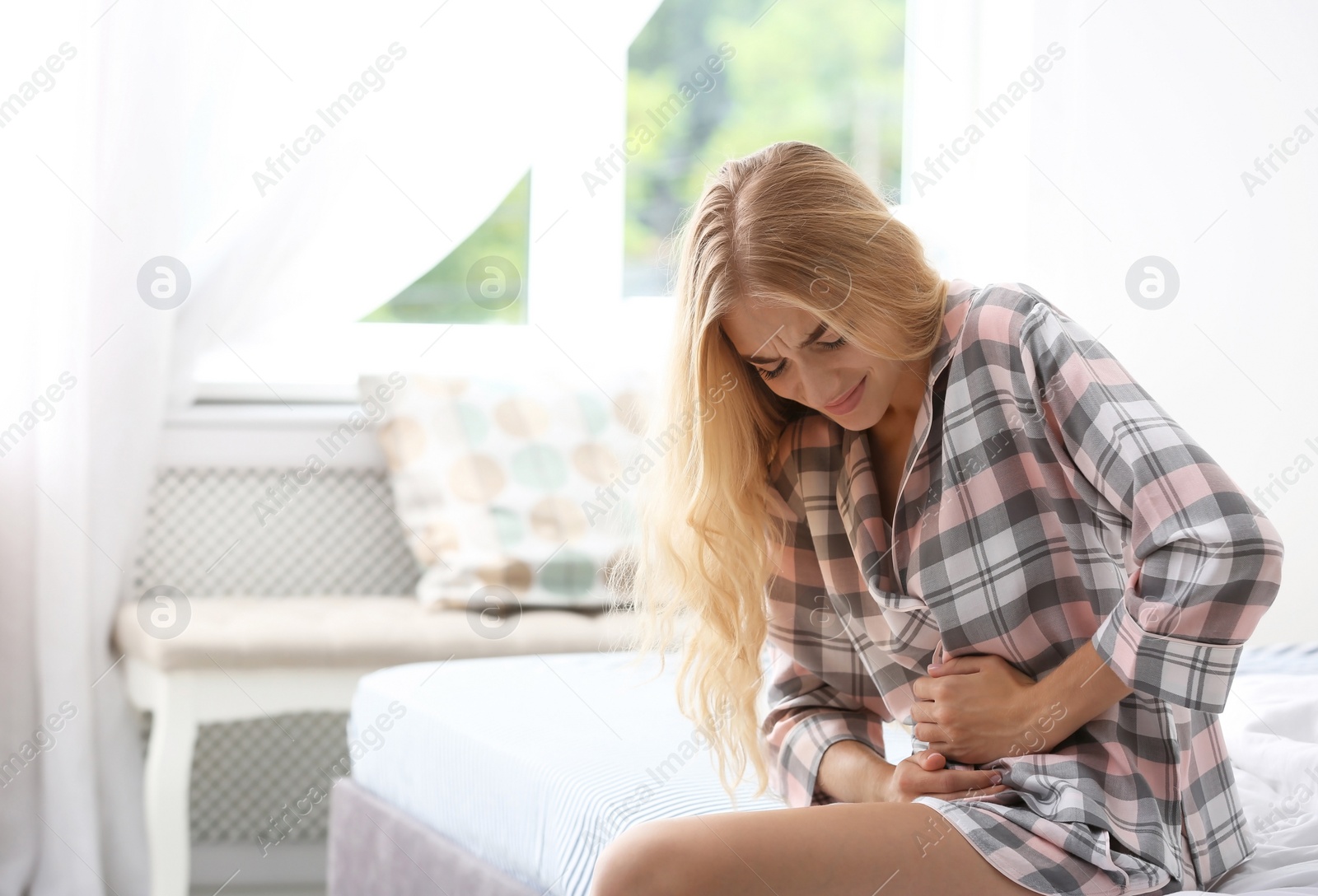 Photo of Young woman suffering from pain in bedroom. Gynecology concept