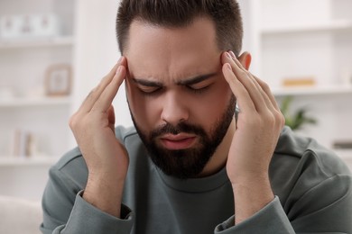 Photo of Man suffering from headache at home, closeup