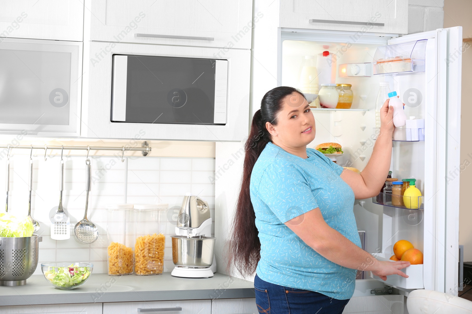 Photo of Overweight woman taking yogurt from refrigerator in kitchen, space for text. Healthy diet