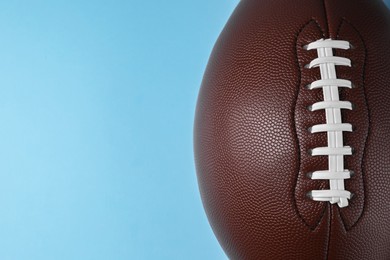 Photo of American football ball on light blue background, top view. Space for text