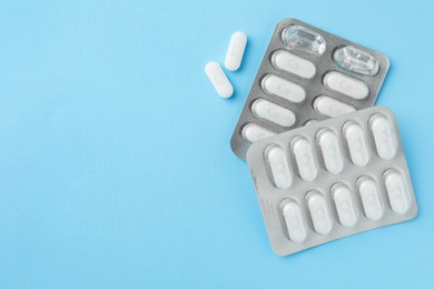 Photo of Blister packs with calcium supplement pills on light blue background, flat lay. Space for text
