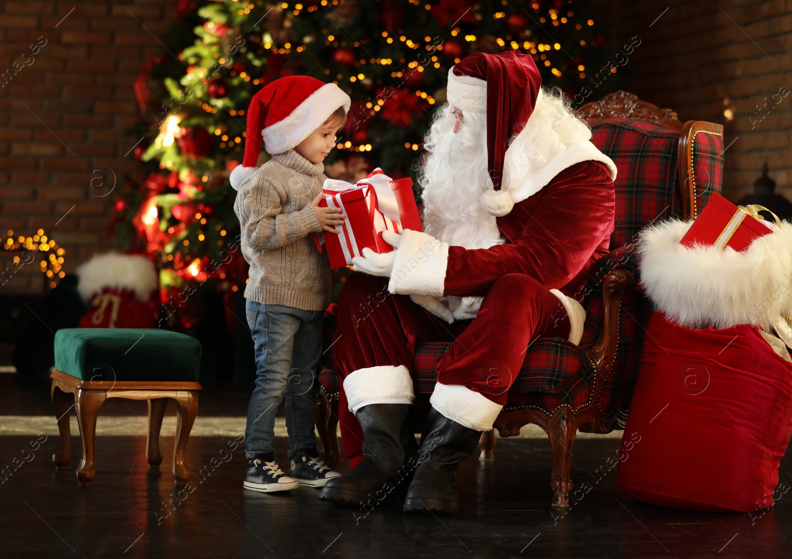 Photo of Santa Claus and little boy with gift near Christmas tree indoors