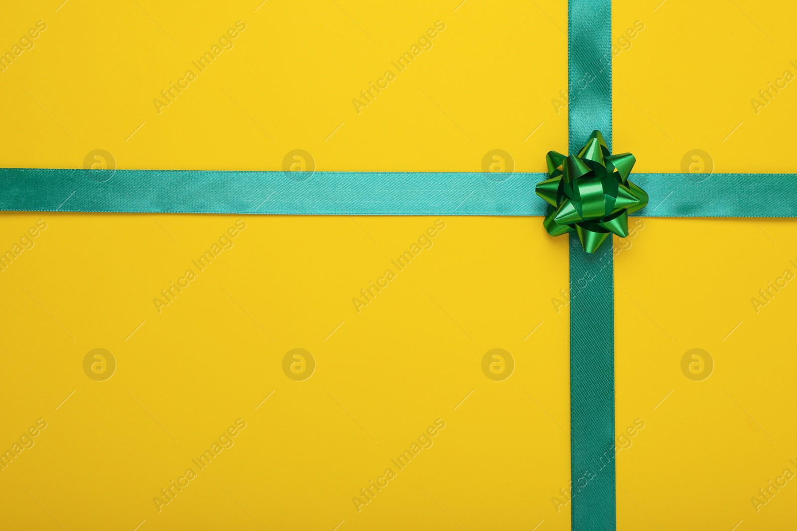 Photo of Green ribbons with bow on yellow background, top view. Space for text