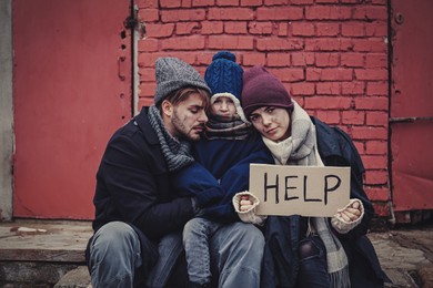 Poor young family with HELP sign on dirty street