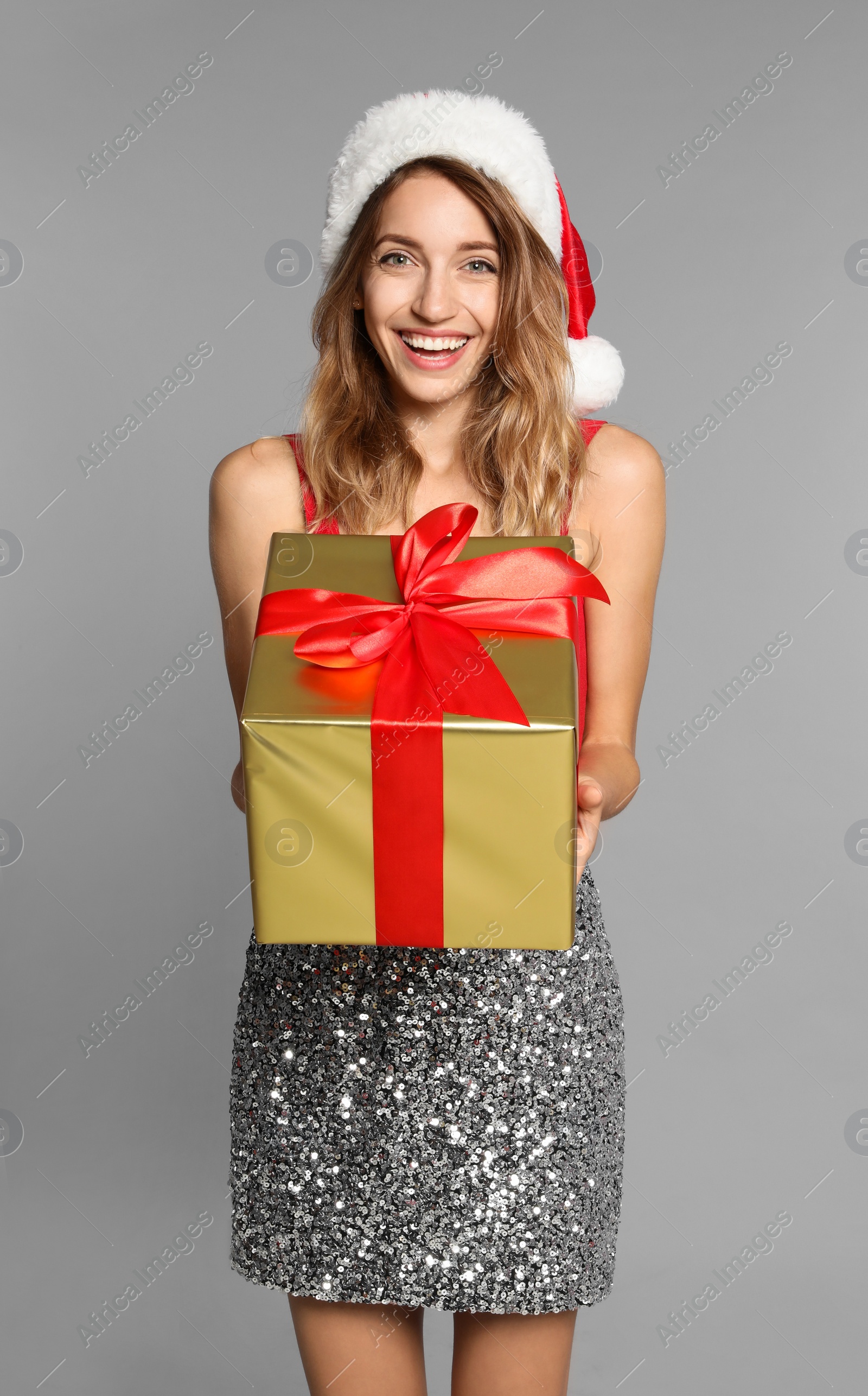 Photo of Happy young woman in Santa hat with gift box on light grey background. Christmas celebration