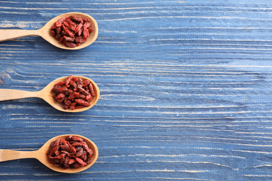 Photo of Dried goji berries in spoons on blue wooden table, flat lay. Space for text