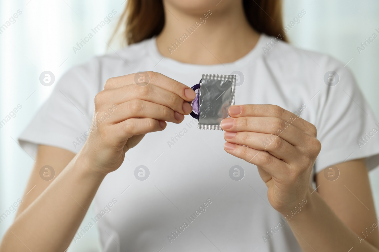 Photo of Woman pulling condom out from package indoors, closeup. Safe sex