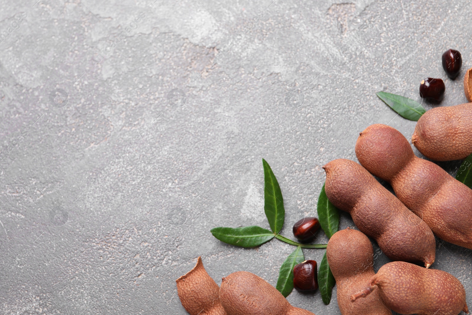 Photo of Ripe tamarinds and fresh leaves on grey table, flat lay. Space for text