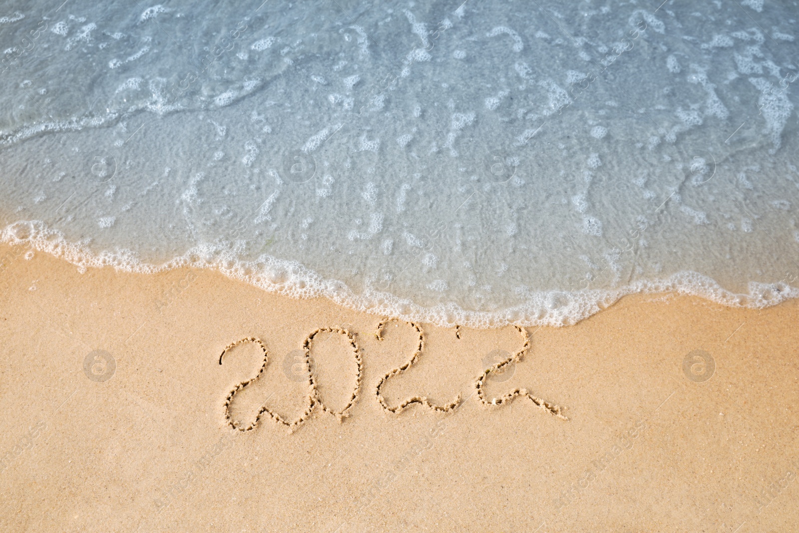 Photo of Sandy beach with written 2022 washed by sea. Happy New Year, above view