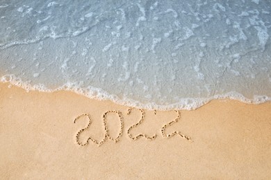 Photo of Sandy beach with written 2022 washed by sea. Happy New Year, above view