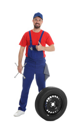 Full length portrait of professional auto mechanic with lug wrench and wheel on white background