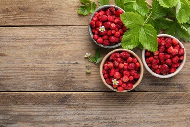 Photo of Fresh wild strawberries in bowls and leaves on wooden table, flat lay. Space for text