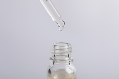 Dripping cosmetic serum from pipette into bottle on light grey background