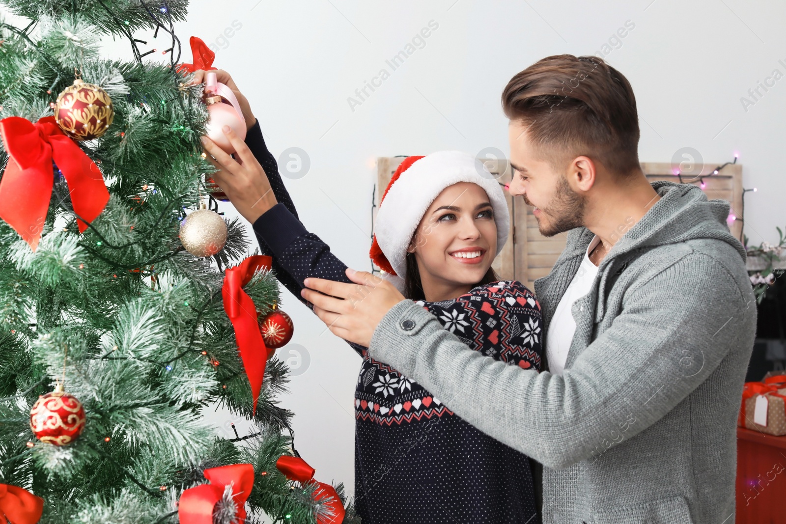 Photo of Happy young couple decorating Christmas tree together at home