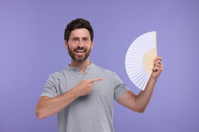 Happy man holding hand fan on purple background