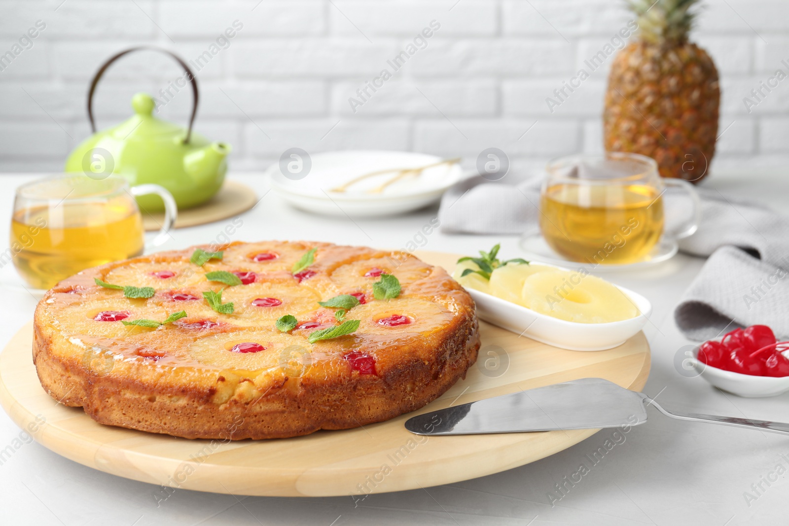 Photo of Tasty pineapple cake with cherries and mint on white table