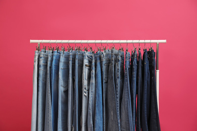 Photo of Rack with stylish jeans on pink background