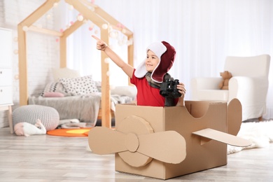 Photo of Cute little boy playing with binoculars and cardboard airplane in bedroom