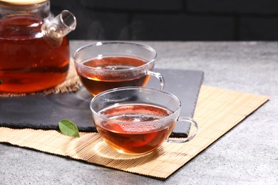 Photo of Aromatic hot tea in glass cups and teapot on light grey table
