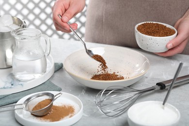 Photo of Making dalgona coffee. Woman pouring instant granules into bowl at light gray table, closeup