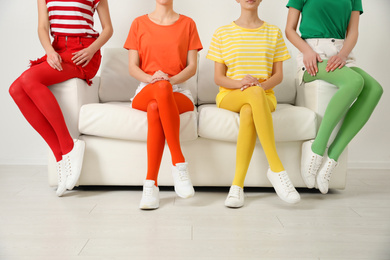 Women wearing bright tights sitting on sofa indoors, closeup